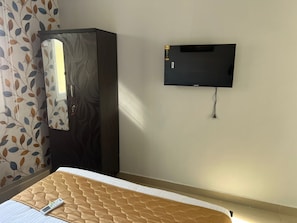 A room with a bed, a wardrobe, a television mounted on the wall, and a window with curtains. - Aerodon resort (Tirupporur)