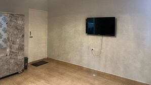 A room with a flat-screen TV mounted on the wall, a ceiling fan, and a wooden floor. - Aerodon resort (Tirupporur)