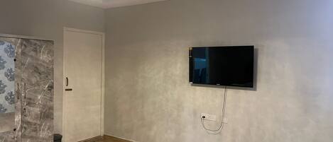 A room with a flat-screen TV mounted on the wall, a ceiling fan, and a wooden floor.