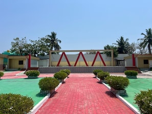 A courtyard with a red brick pathway, a geometric wall structure, and greenery. - Aerodon resort (Tirupporur)