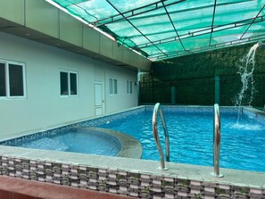 Une piscine dotée d’un toit végétalisé, d’une fontaine et d’une bordure carrelée.