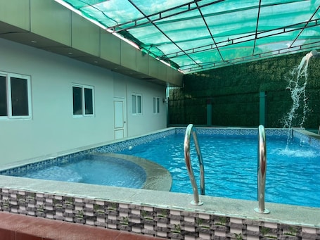 A swimming pool with a green roof, a water fountain, and a tiled edge.. Aerodon resort