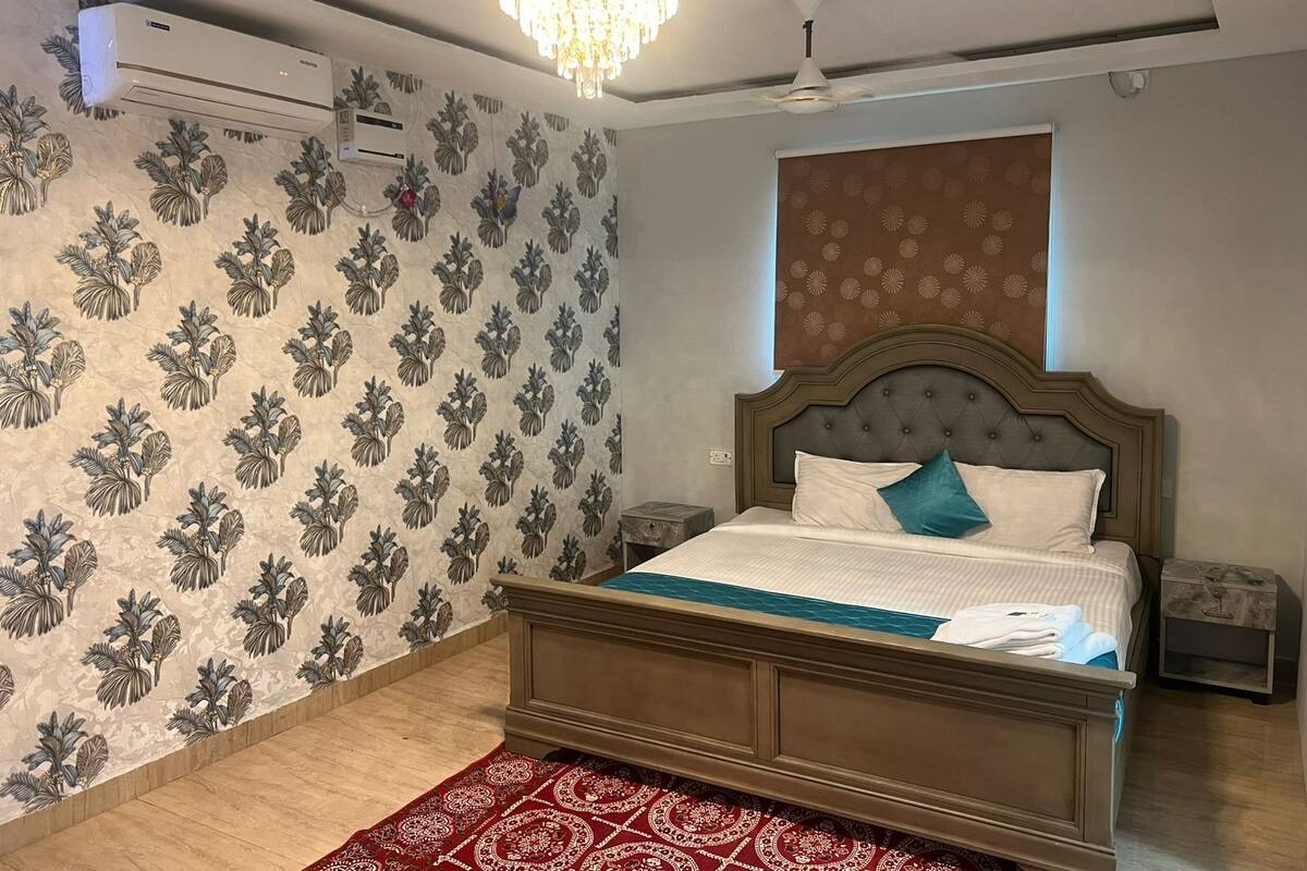 A bedroom with a bed, a chandelier, an air conditioner, and patterned wallpaper.