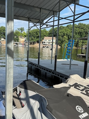 Ein überdachter Steg mit einer Leiter, einem Boot und einem Haus im Hintergrund.