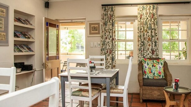 A room with a dining table, chairs, a wicker sofa, a small round table, and a bookshelf.
