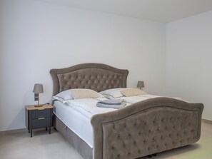 Ein Bett mit gestepptem Kopfteil, ein Nachttisch mit Lampe und eine Kommode.