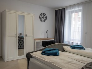 Ein Schlafzimmer mit Bett, Kleiderschrank, Schreibtisch, Lampe und einer Wanduhr.