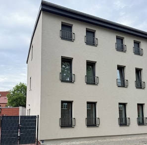A multi-story building with a flat facade, multiple windows with black railings, and a visible door. - Modern apartment with 2 bedrooms for up to 6 guests (wittenberge)