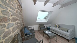 Une pièce avec un mur en pierre, un plafond en pente, une fenêtre, un canapé, un fauteuil et une petite table.