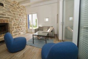 A living room with a stone wall, a fireplace, a sofa, a coffee table, and a sliding glass door. - 8 min. walk from the beach - Charming house (10 p.) - in a green setting (Plouhinec)