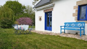 Un bâtiment blanc avec une porte et une fenêtre bleues, un banc et une table avec des chaises à l’extérieur.