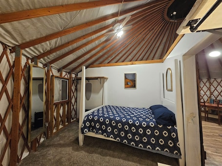 A bedroom with a bed, a ceiling fan, a window, and a door.. Dragonfly Yurt glamping