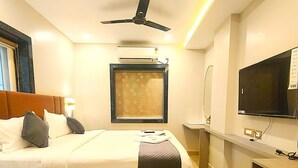 Une chambre d’hôtel équipée d’un lit, d’une table de chevet, d’un téléviseur, d’un climatiseur et d’un ventilateur de plafond.