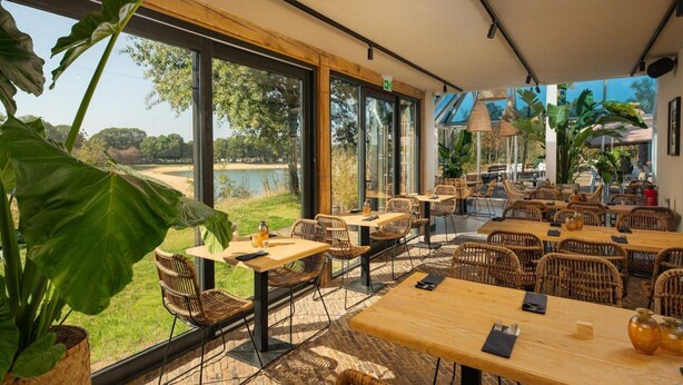 A restaurant with outdoor seating, large windows, and a view of a lake. - Holiday Home in Wilsum With Hottub (Wilsum)