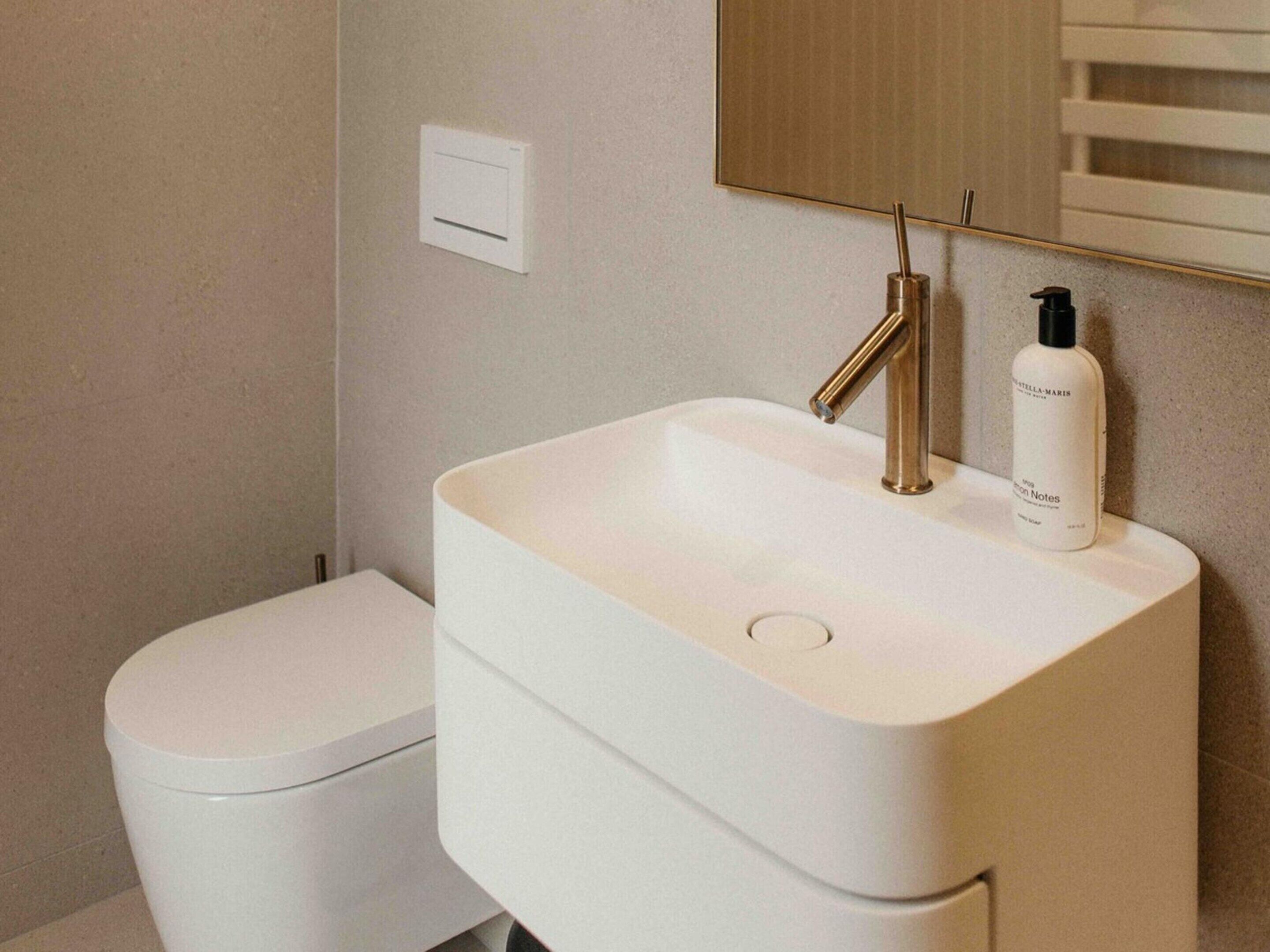 Une salle de bain avec un lavabo blanc, un robinet doré et un flacon de lotion posé sur le comptoir.