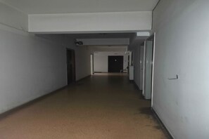 A long, narrow hallway with white walls and a brown floor, leading to a door at the end. - Modern Studio l Worn Bldg Entrance (Athina)