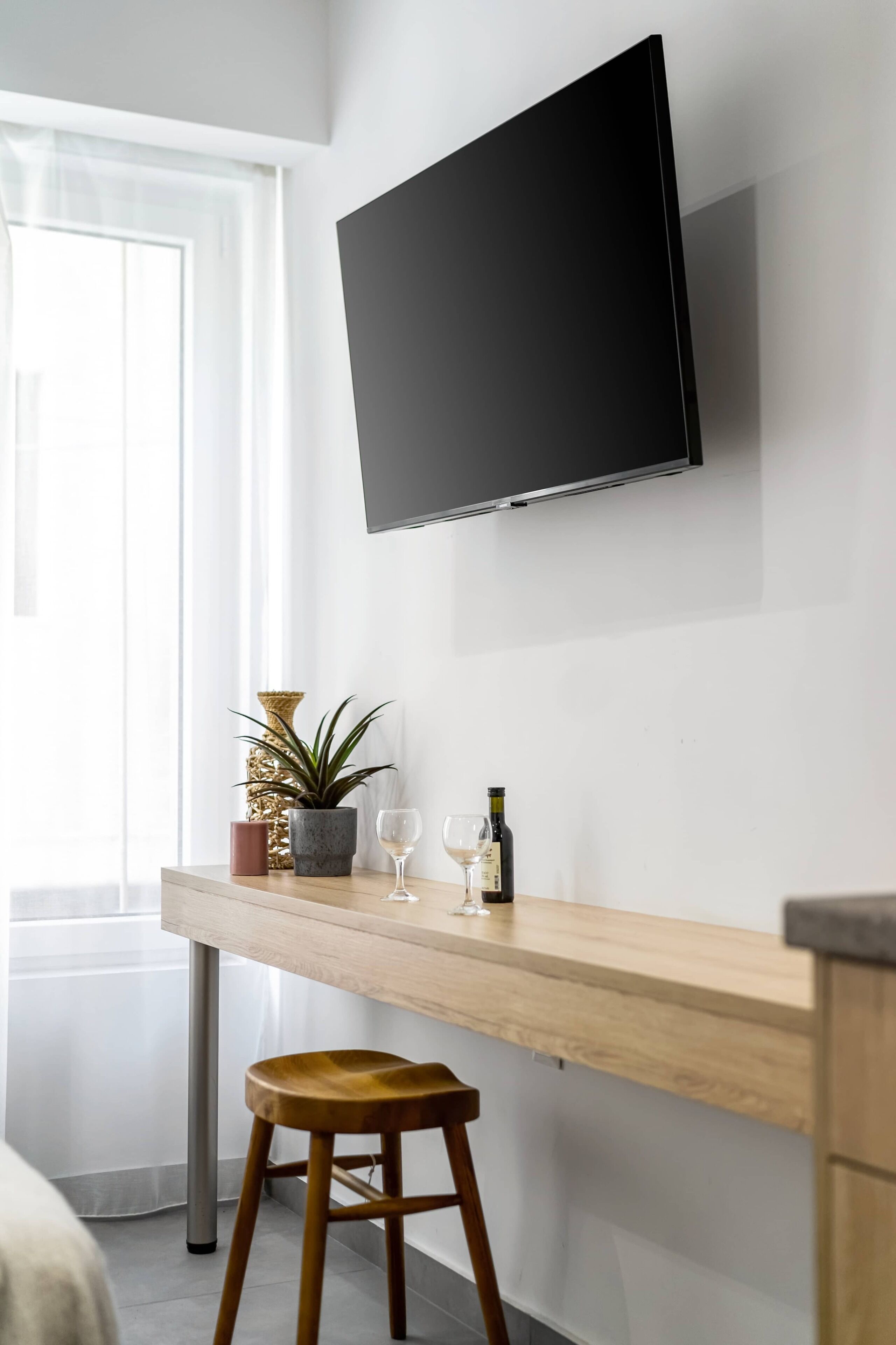 Een moderne kamer met een houten bureau, een wandgemonteerde televisie, een potplant, een wijnglas en een fles.