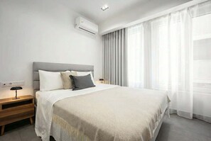A modern hotel room with a large bed, a bedside table, an air conditioning unit, and sheer curtains. - Modern Studio l Worn Bldg Entrance (Athina)