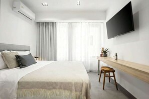 A modern hotel room with a bed, a TV mounted on the wall, a desk with a stool, and a window with curtains. - Modern Studio l Worn Bldg Entrance (Athina)