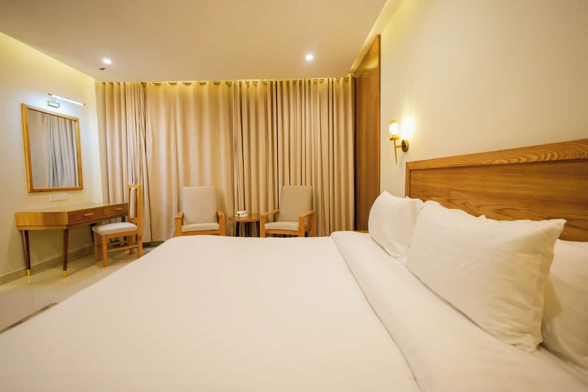 A hotel room with a large bed, a desk, two chairs, a mirror, and a curtain.
