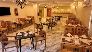 Un restaurante con suelo de mármol, mesas y sillas de madera e iluminación colgante.