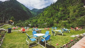 A terrace with outdoor seating, surrounded by lush greenery and mountains.