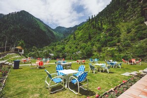 A terrace with outdoor seating, surrounded by lush greenery and mountains. - Hotel One Riverside Kaghan (Balakot)