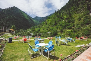 A terrace with outdoor seating, surrounded by lush greenery and mountains.