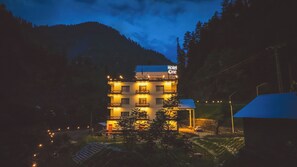 Un hôtel à plusieurs étages doté de balcons, une enseigne indiquant « Hôtel One », et un paysage montagneux en arrière-plan.