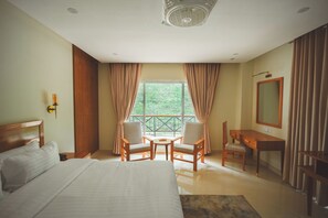 Une chambre dâhĂŽtel avec un lit, deux chaises, un bureau, un miroir et une fenĂȘtre avec des rideaux.