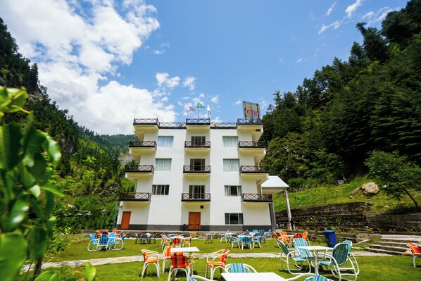 A multi-story hotel with outdoor seating and a mountain backdrop.
