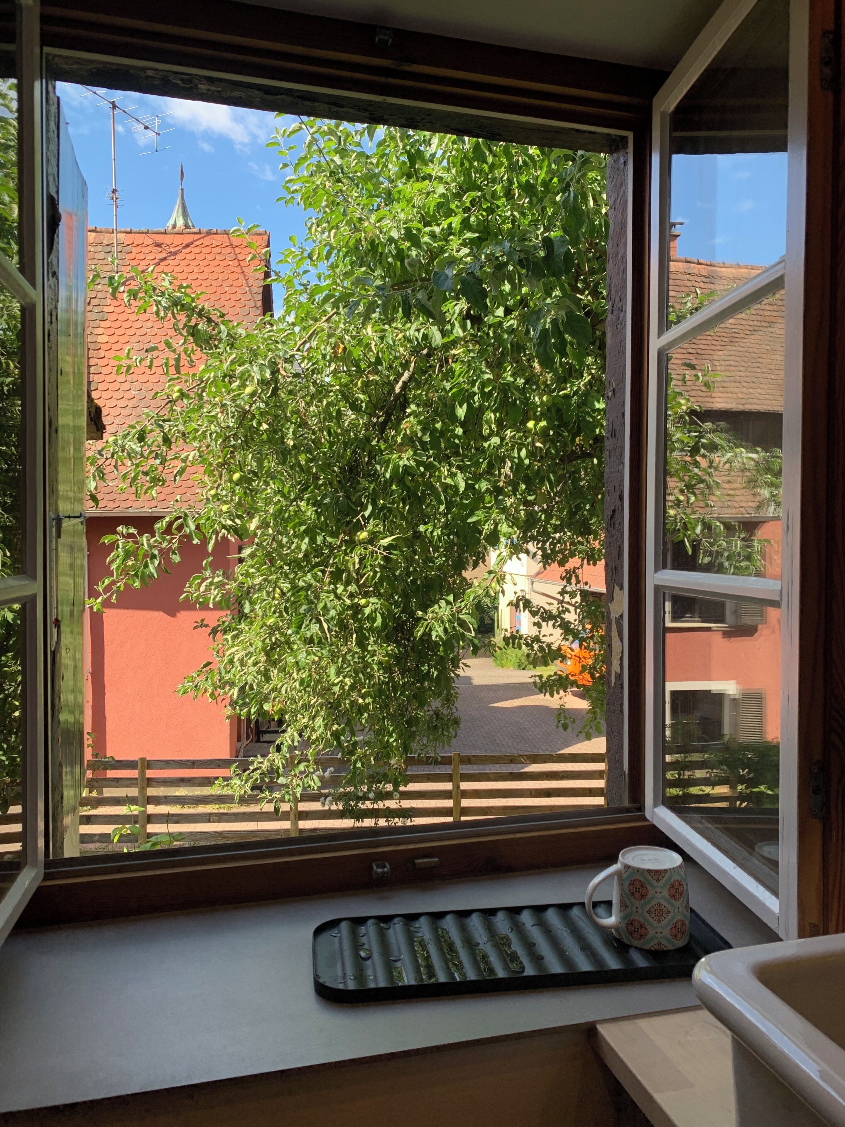 Ein Fenster mit Blick auf einen Baum und Gebäude, eine Tastatur und eine Tasse auf einem Fensterbrett.