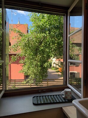 A window with a view of a tree and buildings, a keyboard, and a mug on a windowsill. - Quiet and Central Location in a Historic House with a Variety of Excursions (Kandern)