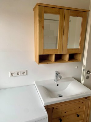 A bathroom with a white sink, wooden cabinet, and mirror. - Quiet and central in a historic house with a variety of excursion destinations (Kandern)