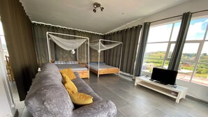 A modern bedroom with a large bed, a sofa, a TV, and a view of the outdoors. - Apartment with 360-degree view (Antananarivo)