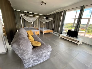 A modern bedroom with a large bed, a sofa, a TV, and a view of the outdoors.