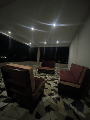 A rooftop terrace with two sofas, a patterned floor, and a night view.
