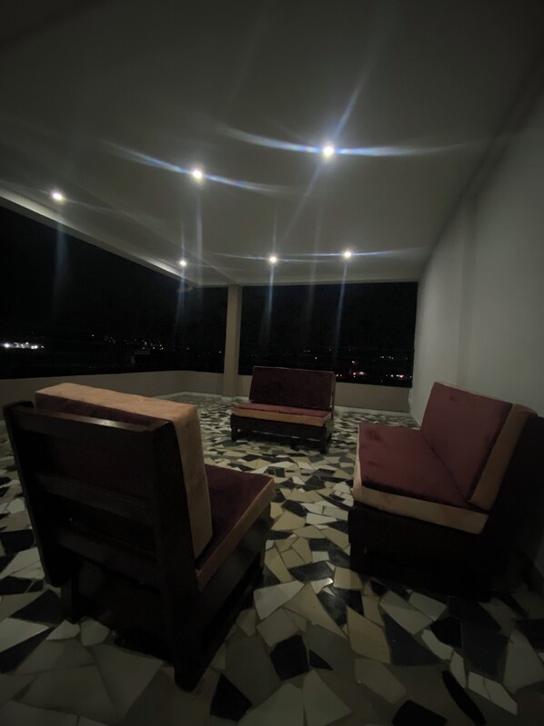 A rooftop terrace with two sofas, a patterned floor, and a night view.