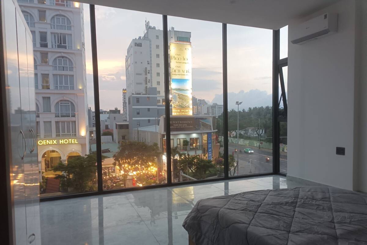 A modern hotel room with a large window, a bed, and a view of the cityscape.