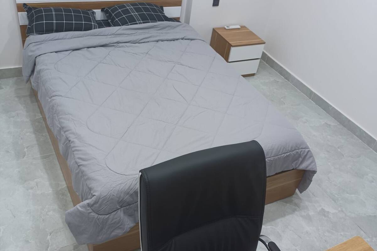 A bedroom with a bed, a nightstand, a desk, and a chair.