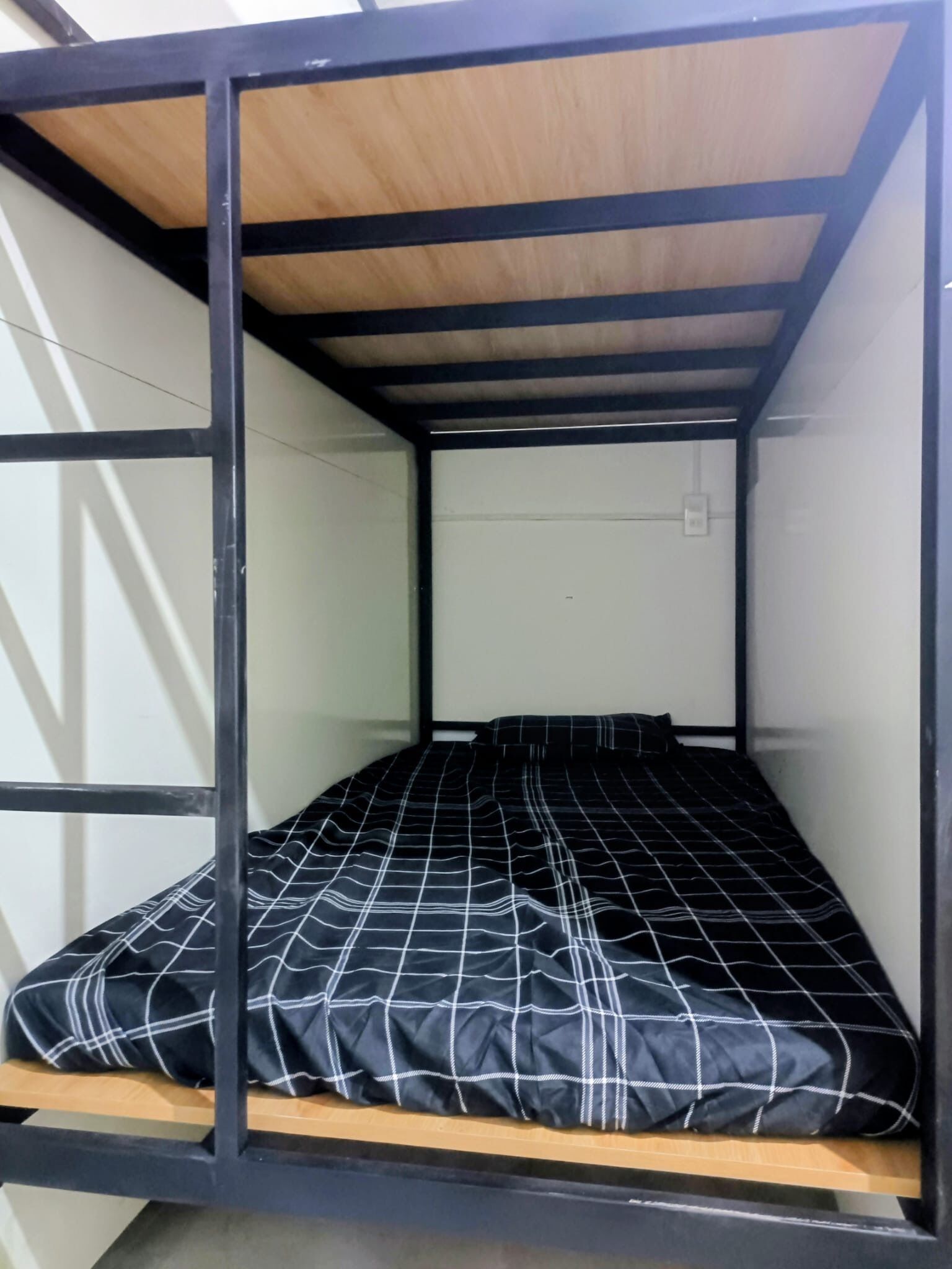 A bunk bed with a black and white checkered bedspread, wooden headboard, and metal frame.