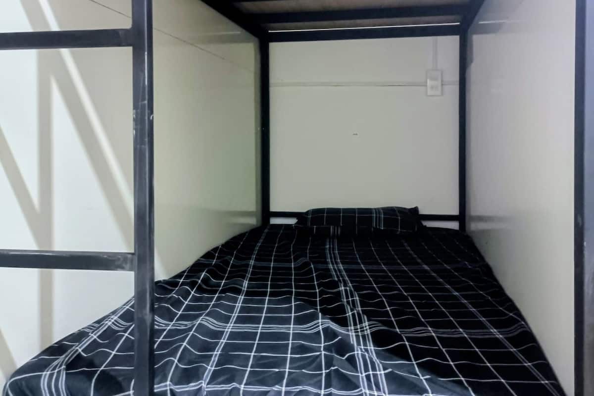 Una cama litera con colcha a cuadros blanco y negro, cabecera de madera y estructura metálica.