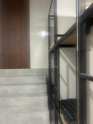 Una cama litera con estructura metálica, escalones de piedra gris y un panel de madera a la izquierda.