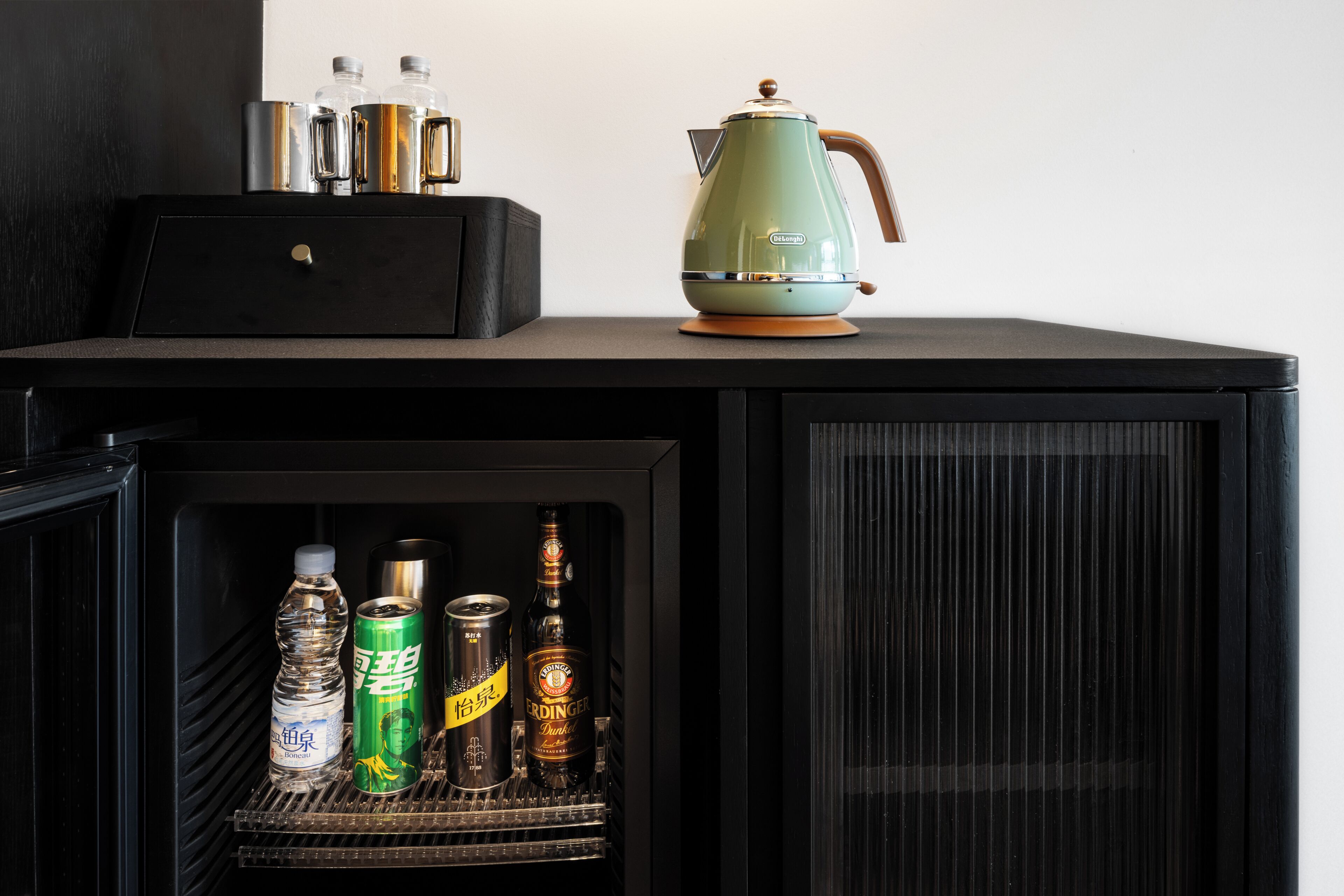 Un minibar con un hervidor verde, botellas y latas.