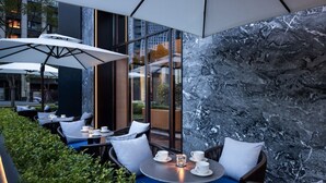 An outdoor seating area with tables and chairs, a glass wall, and a marble wall. - Intercity Hotel Chengdu High tech Center (Chengdu)