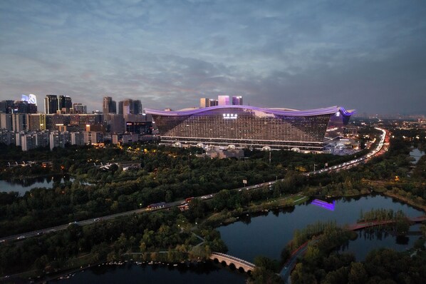 Un grand bâtiment moderne doté d’une architecture de toit originale, entouré d’une rivière et d’un paysage urbain.