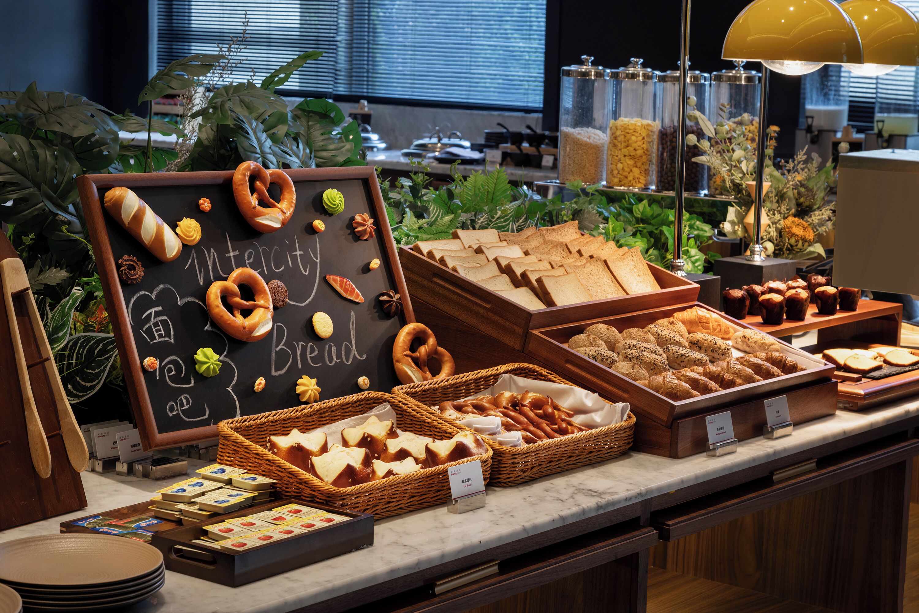 Monipuolinen buffet, jossa on tarjolla erilaisia leipiä, leivonnaisia ja liitutaululle kirjoitettu ruokalista.