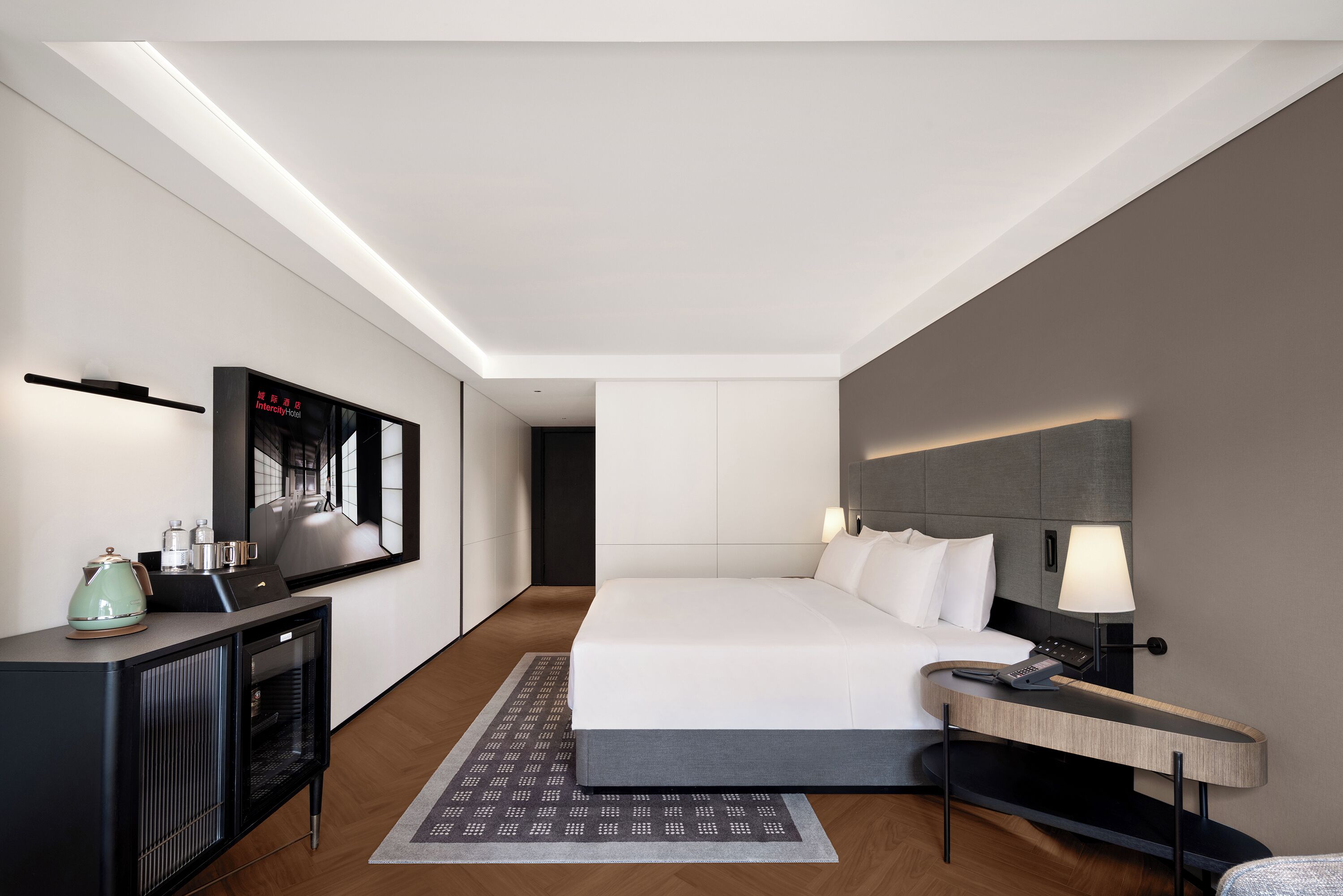 A modern hotel room with a large bed, bedside table, lamp, and a flat-screen TV.