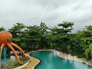 Ein Swimmingpool mit einer großen Oktopusskulptur, umgeben von üppiger Vegetation.