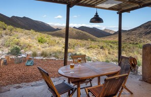 Un área de estar al aire libre con una mesa, sillas, una lámpara colgante y vistas a las montañas.